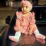 baby, car_hood, child, curious, cute, expression, fashion, feet, headband, knitted_clothing, night, outdoor, person, pink_dress, portrait, reflection, sitting, toddler, warm_clothing, young_child
