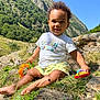 Hélio a rejoint le concours — aidez-le/la à gagner de superbes lots ! child, toddler, smiling, grass, rocks, mountain, outdoor, nature, sunlight, blue_sky, toy, shorts, tshirt, barefoot, happy, sitting, greenery, daylight, curly_hair, play