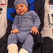 Líam Mauricio Susman joined the competition — help win amazing prizes! baby, infant, child, blue_clothing, hat, socks, blanket, couch, smile, winking, indoors, cozy, cute, person, portrait, seated, hand, footwear, fabric, relaxing