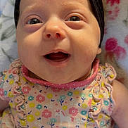 Stormi joined the competition — help win amazing prizes! baby, black, blanket, blue, bow, child, closeup, cute, dress, face, floral_pattern, flower_pattern, happy, headband, infant, lying_down, pink, skin, smiling, yellow