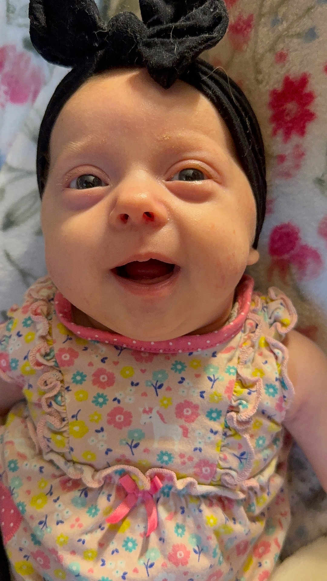 Stormi joined the competition — help win amazing prizes! baby, black, blanket, blue, bow, child, closeup, cute, dress, face, floral_pattern, flower_pattern, happy, headband, infant, lying_down, pink, skin, smiling, yellow