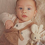 Leni is registered to the contest to win money with this photo: baby, infant, blue_eyes, knitted_toy, bunny, rattle, beige_clothing, overalls, blanket, soft_texture, portrait, cute, child, indoor, closeup, young_child, cozy, hand, face, lying_down