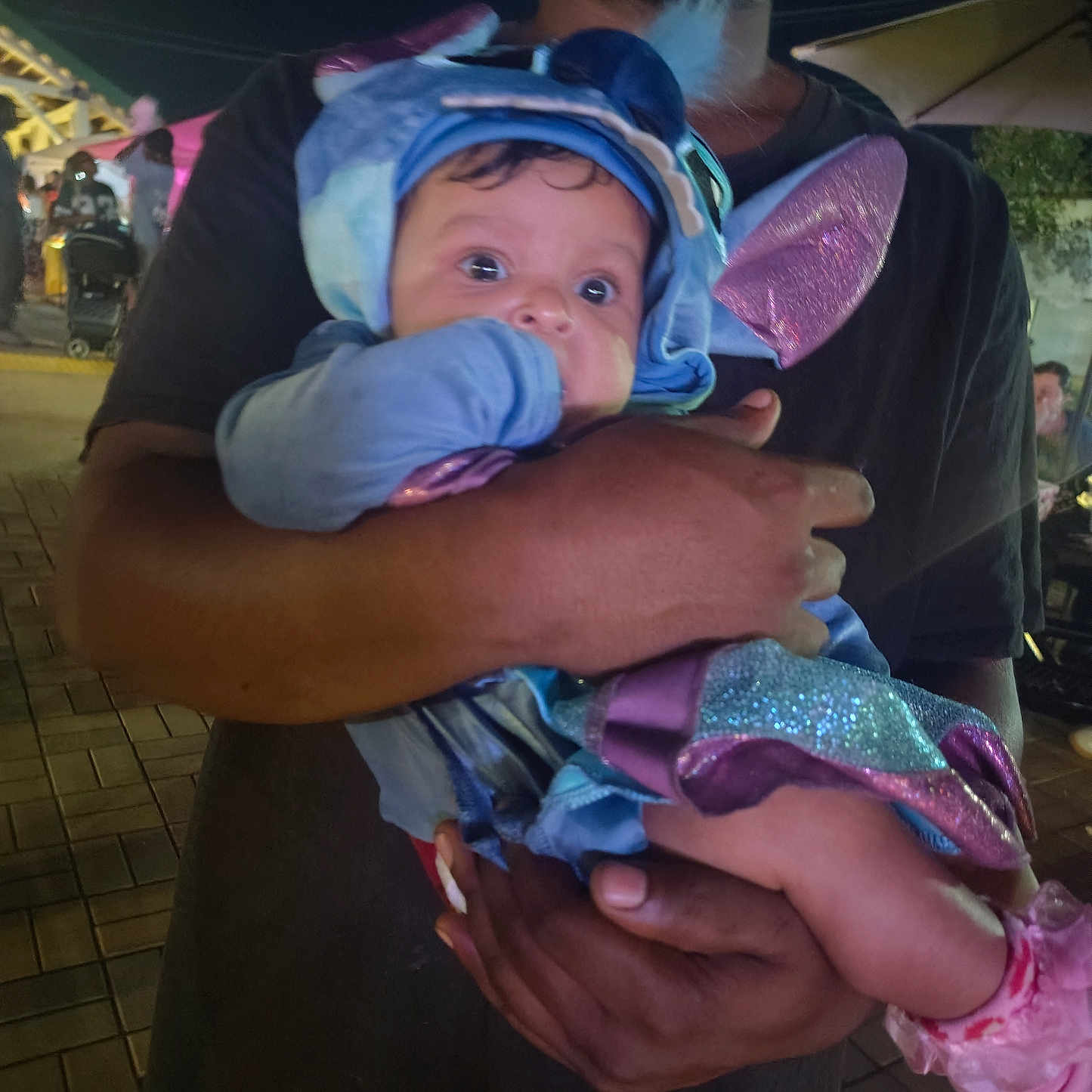 Malia joined the competition — help win amazing prizes! baby, child, infant, costume, blue, purple, sparkly, hat, wings, smiling, wide_eyed, portrait, being_held, adult, parent, nighttime, outdoor, event, crowd, pavement