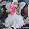 baby, infant, child, angel_costume, wings, headband, tutu, bib, pink_clothing, bunny_slippers, smiling, portrait, car, vehicle, adult, caregiver, outdoor, costume, fluffy, sparkles