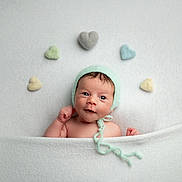 Eliott participe au concours pour gagner de l'argent avec cette photo : baby, infant, newborn, blanket, knitted_hat, heart_shapes, soft_texture, pastel_colors, cute, portrait, smiling, headwear, lying_down, cozy, child, innocence, warmth, white_background, peaceful, adorable