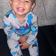 Junior is registered to the contest to win money with this photo: child, toddler, smiling, happy, portrait, sitting, pajamas, cartoon, colorful_clothing, bare_feet, couch, indoor, home, face, teeth, dark_hair, flash_photography, close_up, family, playful
