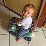 toddler, child, toy_car, indoor, barefoot, blue_eyes, red_hair, steering_wheel, tile_floor, curious, looking_up, white_shirt, blue_pants, small_vehicle, playtime, home, door, wooden_frame, floor_tiles, baby