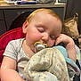 baby, sleeping, pacifier, blanket, indoor, child, red_seat, kitchen, face, arm, hand, clothing, furniture, soft_toy, peaceful, nap, light, cute, comfort, young_child
