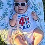baby, infant, sunglasses, smiling, onesie, clothing, blanket, grass, outdoor, celebration, holiday, summer, cute, happy, portrait, child, sunlight, skin, face, lying_down