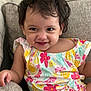 Fatima is registered to the contest to win money with this photo: toddler, child, smiling, happy, sitting, couch, clothing, floral_pattern, colorful, hair, face, portrait, indoors, cute, young_child, person, apparel, skin, eyes, expression