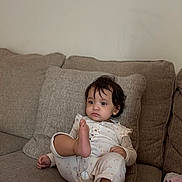 Fatima is registered to the contest to win money with this photo: toddler, child, pajamas, couch, sofa, indoor, face, foot, curly_hair, blanket, neutral_expression, home, furniture, comfort, relaxing, infant, person, seated, cozy, casual