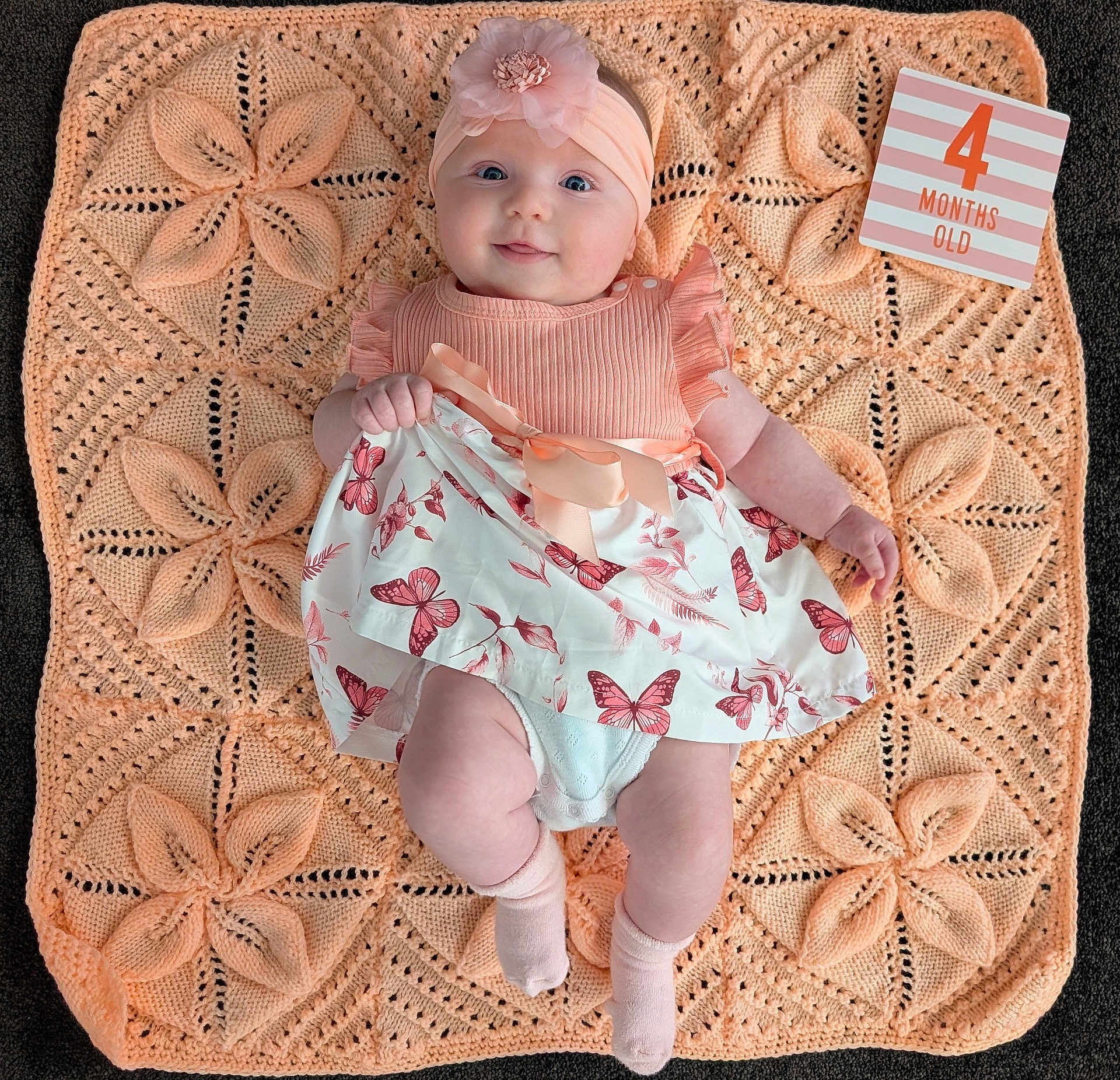 Luna joined the competition — help win amazing prizes! baby, infant, child, smiling, dress, headband, blanket, knitted, milestone_card, 4_months_old, butterfly_pattern, pink, peach, cute, happy, socks, lying_down, portrait, indoor, person