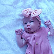 Rayne is registered to the contest to win money with this photo: baby, infant, pink_bow, headband, pink_outfit, blanket, lying_down, cute, expression, fists, newborn, child, soft_texture, indoors, portrait, adorable, small_hands, clothing, headwear, resting