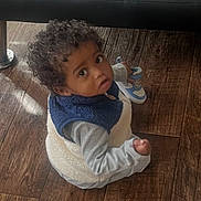 Zyaire joined the competition — help win amazing prizes! toddler, child, curly_hair, sitting, wooden_floor, shoe, blue_shoe, white_shoe, vest, long_sleeve, indoor, person, looking_up, curious, cute, small_hand, flooring, casual_clothing, baby, footwear