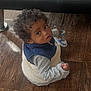toddler, child, curly_hair, sitting, wooden_floor, shoe, blue_shoe, white_shoe, vest, long_sleeve, indoor, person, looking_up, curious, cute, small_hand, flooring, casual_clothing, baby, footwear