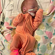 Ella is registered to the contest to win money with this photo: newborn, baby, infant, onesie, orange_clothing, blanket, medical_tubes, nasal_cannula, hospital, bed, sleeping, face, person, healthcare, cute, small, resting, patterned_blanket, pink, yellow