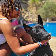 Venom participe au concours pour gagner de l'argent avec cette photo : person, dog, black_dog, pool, outdoor, sunlight, curly_hair, sunglasses, affection, pet, water, summer, relaxation, swimwear, blue_towel, nature, fence, backyard, daytime, happy
