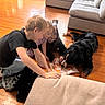 children, dog, reading, book, floor, wooden_floor, couch, indoors, happy, smiling, playful, family, black_dog, casual_clothing, home, interaction, fun, group, child, pet