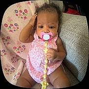 Amaiah is registered to the contest to win money with this photo: baby, pacifier, pink, floral, blanket, couch, infant, child, cute, clothing, sitting, hand, face, indoors, portrait, young, comfortable, expression, holding, relaxation