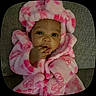 baby, child, pink_robe, heart_pattern, couch, indoor, soft_texture, hand, face, eyes, infant, cute, fluffy, sitting, portrait, cozy, warm_clothing, expression, young_child, closeup