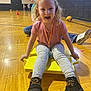 child, blonde_hair, pink_shirt, yellow_scooter, gymnasium, basketball, kids, wooden_floor, play, boots, leggings, sports, indoor, fun, active, smiling, happy, exercise, recreation, leisure