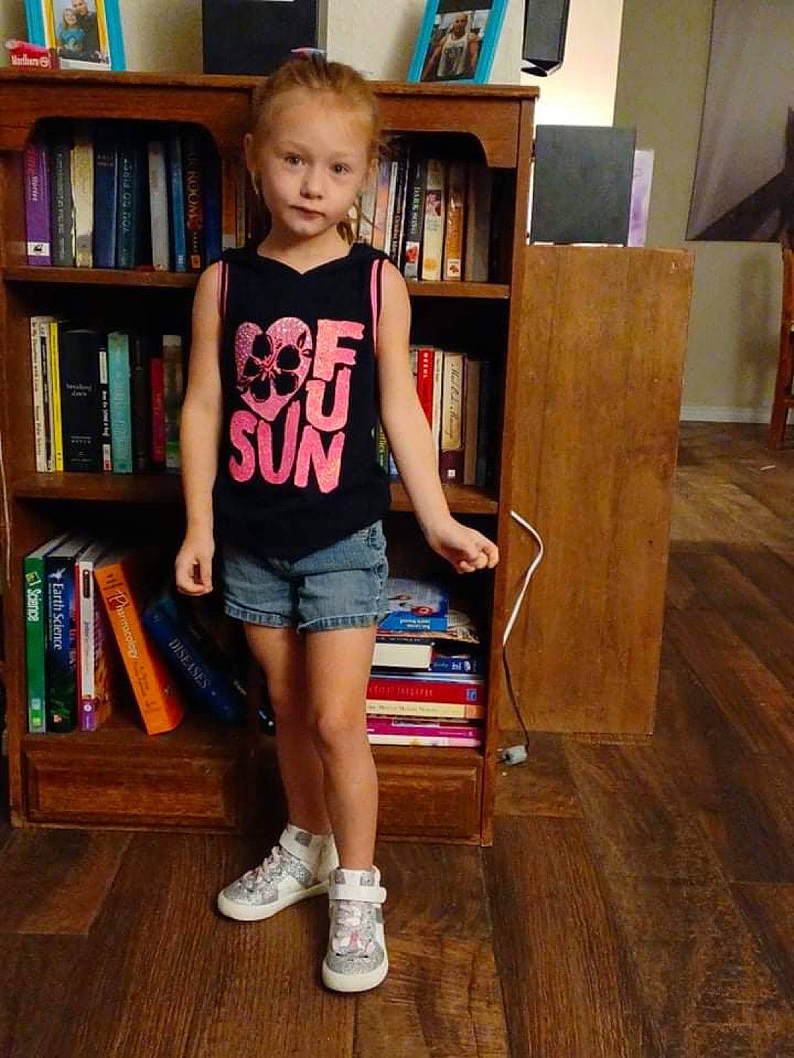 Melina is registered to the contest to win money with this photo: book, bookcase, floor, flooring, furniture, hair, hairstyle, knee, leg, person, publication, shelf, shelving, shorts, sleeve, sneakers, standing, t_shirt, thigh, waist