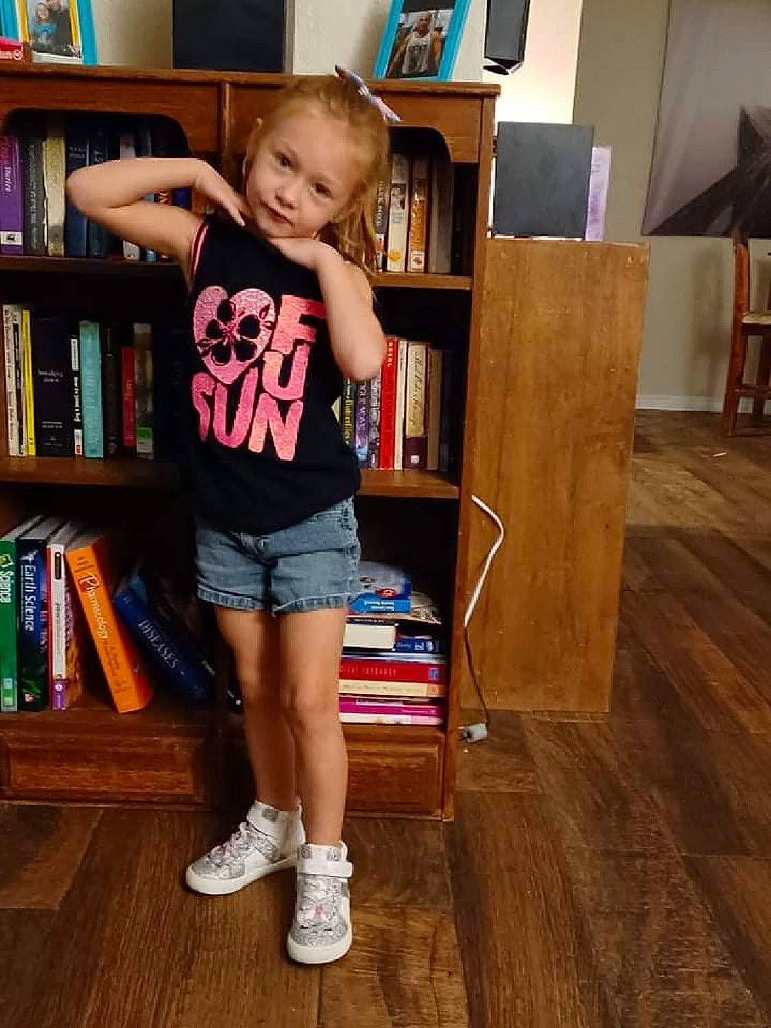 Melina is registered to the contest to win money with this photo: bookcase, child, electric_blue, floor, flooring, fun, hardwood, human_leg, knee, leg, long_hair, person, picture_frame, publication, shelf, shelving, t_shirt, thigh, toddler, waist