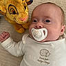 baby, pacifier, plush_toy, lion_toy, soft_surface, white_outfit, cute, infant, child, lying_down, indoors, closeup, face, hand, expression, comfort, toy, clothing, sleepwear, adorable