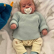 Liam a rejoint le concours — aidez-le/la à gagner de superbes lots ! baby, pacifier, knit_sweater, plush_toy, blanket, star_pattern, toddler, cute, infant, blue_socks, yellow_pants, teddy_bear_print, soft_texture, lying_down, indoors, child, cozy, comfort, face, hand