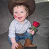 blue_eyes, boots, casual_clothing, child, couch, cowboy_hat, cute, happy, holding_object, home, indoor, lipstick_mark, person, plaid_shirt, portrait, rose, sitting, smiling, toddler, young_child