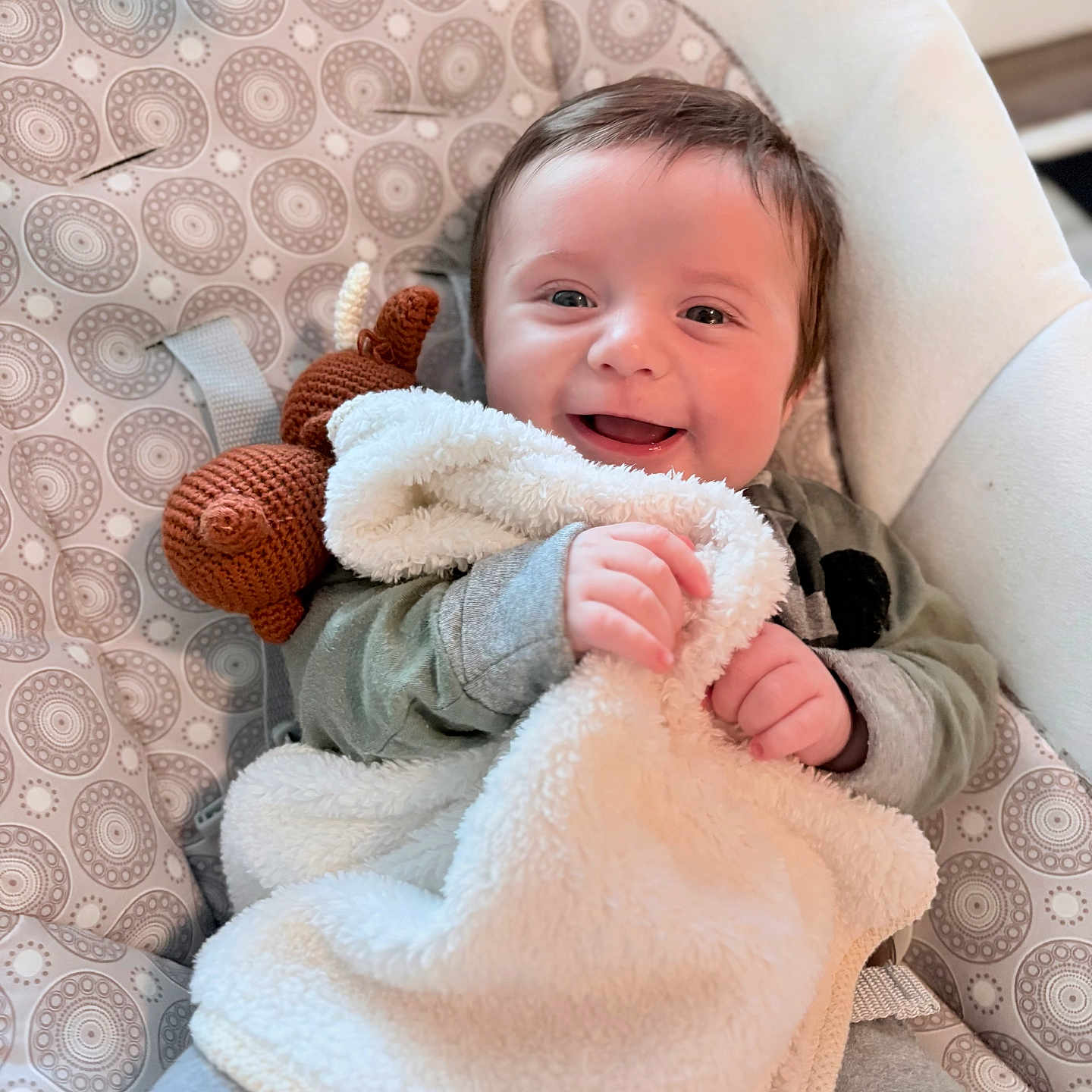 Elijah is registered to the contest to win money with this photo: baby, smiling, blanket, crocheted_toy, baby_seat, patterned_fabric, happy, infant, cute, child, soft_texture, cozy, clothing, hands, face, portrait, indoor, comfort, relaxed, cuddly