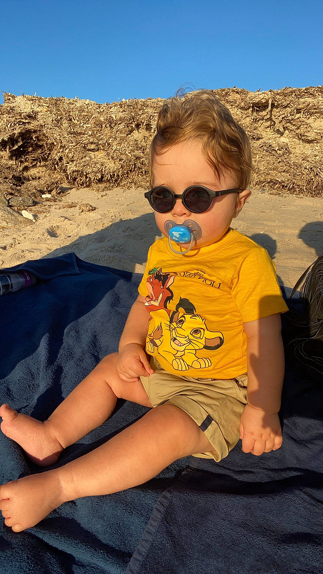 Luca a rejoint le concours — aidez-le/la à gagner de superbes lots ! baby_toddler_clothing, badlands, child, eyewear, foot, glasses, goggles, holiday, lap, person, personal_protective_equipment, sand, sitting, slipper, soil, summer, sunglasses, toddler, toe, vacation