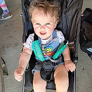 Liam joined the competition — help win amazing prizes! toddler, child, stroller, toy_story, curly_hair, smiling, blue_eyes, casual_clothing, footwear, concrete_floor, cooler, garage, seatbelt, baby, indoor, person, happy, sitting, playful, young_child