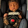 baby, sleeping, car_seat, camouflage, infant, child, seatbelt, safety, cute, hands, headwear, clothing, resting, portrait, indoor, newborn, peaceful, face, person, cozy
