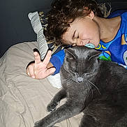 Naël a rejoint le concours — aidez-le/la à gagner de superbes lots ! child, cat, bed, pillow, pacifier, hand, peace_sign, curly_hair, sleepy, cozy, indoor, animal, pet, feline, resting, blue_clothing, neutral_colors, closeup, soft_lighting, relaxation