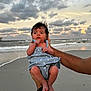 baby, beach, child, clouds, cute, dress, hands, holding, infant, nature, ocean, outdoor, person, portrait, sand, shore, sky, sunset, water, waves