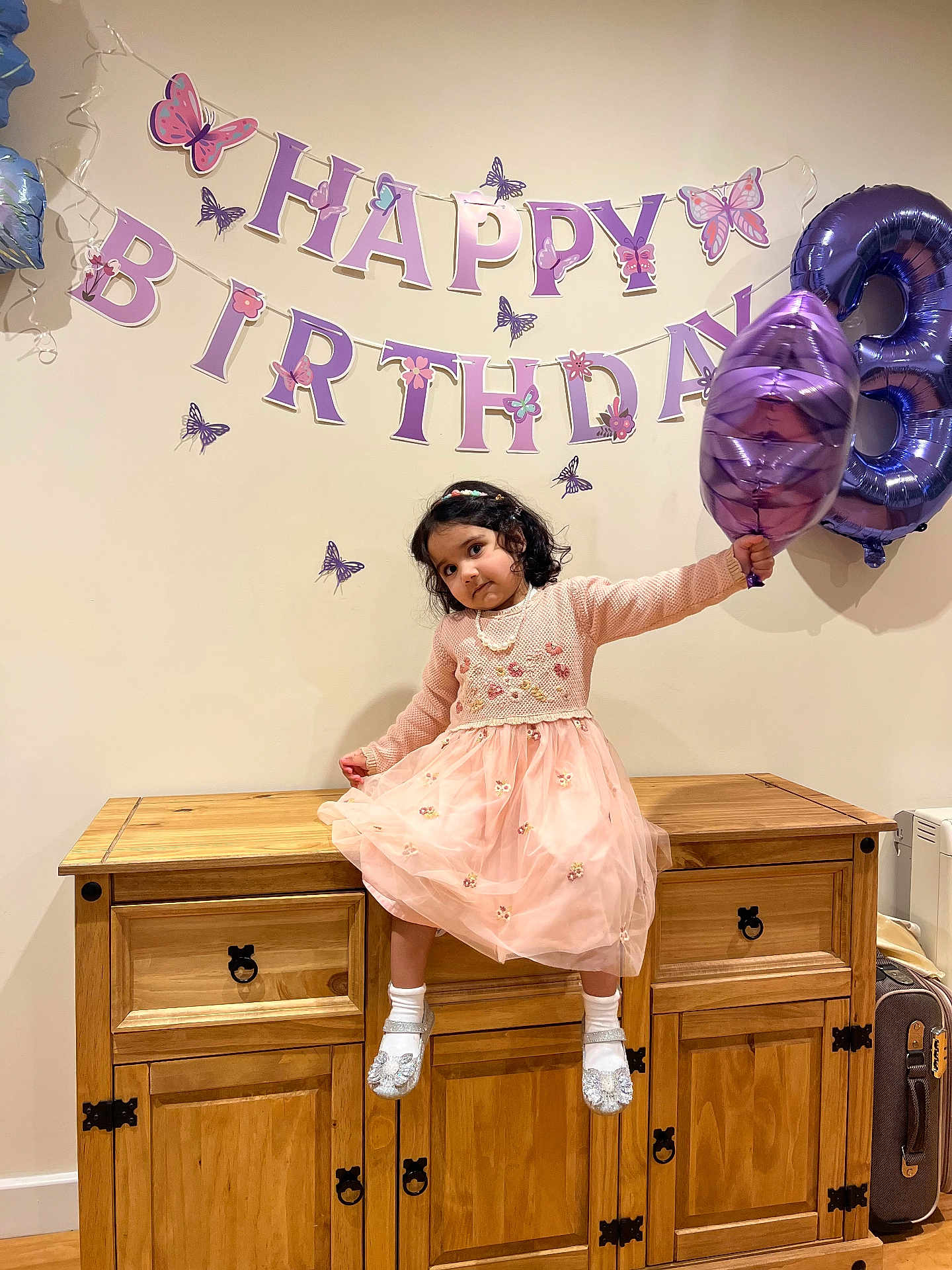 Fatima joined the competition — help win amazing prizes! child, girl, birthday, balloon, number_three, pink_dress, cabinet, wooden_furniture, party_decoration, banner, butterflies, celebration, socks, shoes, indoor, smiling, curly_hair, necklace, wall, festive