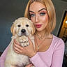 Buddy a rejoint le concours — aidez-le/la à gagner de superbes lots ! woman, puppy, dog, pet, portrait, indoor, blonde_hair, pink_top, necklace, cute, fluffy, holding, looking_at_camera, face, hands, cozy, young_adult, makeup, warm_lighting, casual