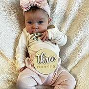 Madilyn is registered to the contest to win money with this photo: baby, infant, child, headband, bow, clothing, pink, blanket, soft_texture, milestone, sign, wooden_sign, cute, portrait, sitting, indoors, person, face, expression, cozy
