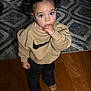 Mia joined the competition — help win amazing prizes! toddler, child, curly_hair, pigtails, blue_eyes, sweatshirt, nike_logo, thumb_sucking, standing, wooden_floor, rug, indoor, boots, pants, casual_clothing, cute, portrait, young_child, home, curious