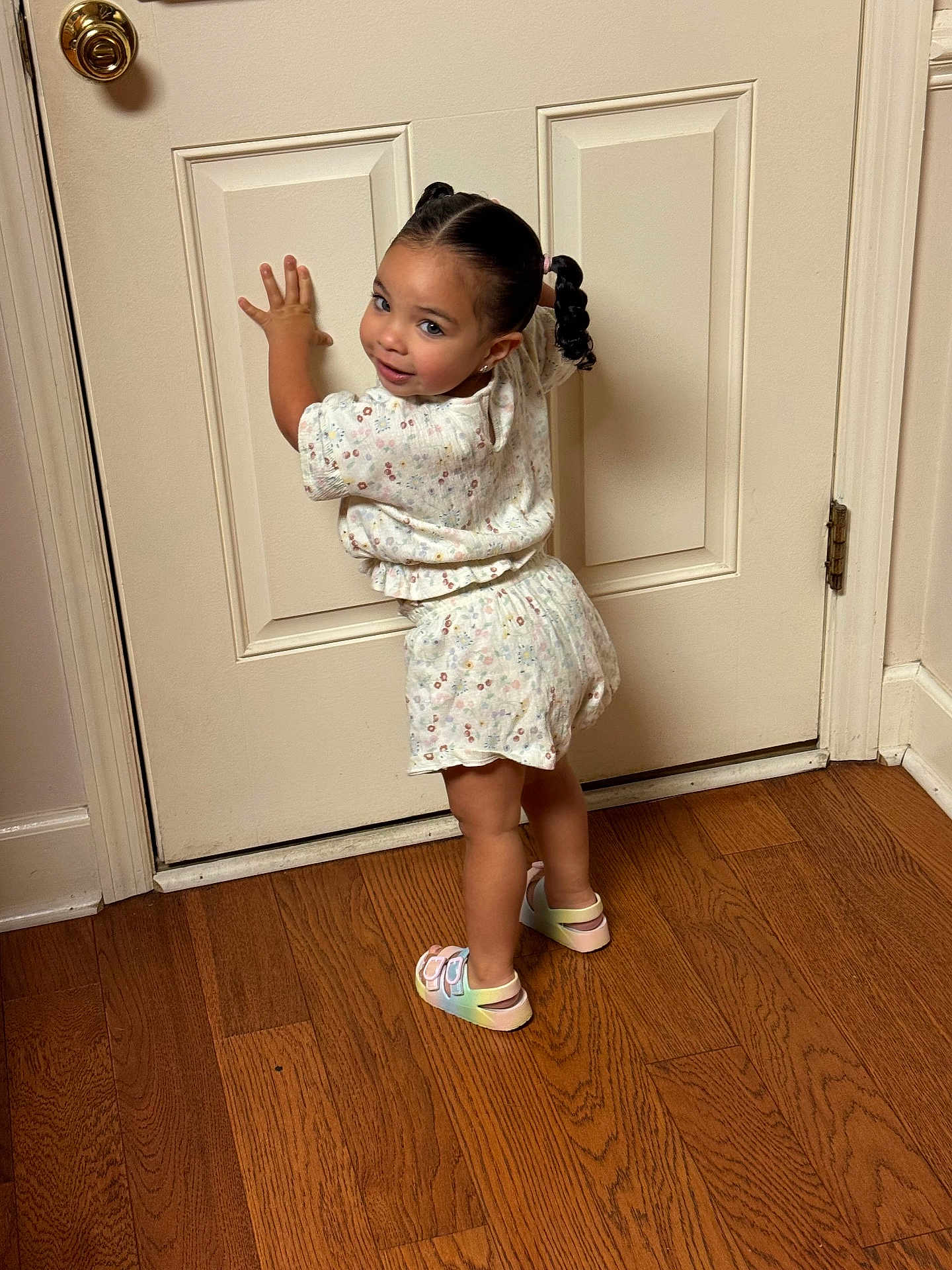 Mia joined the competition — help win amazing prizes! toddler, child, pigtails, smile, standing, door, wooden_floor, indoor, clothing, sandals, hair, playful, person, young_child, wall, flooring, home, cute, fashion, girl