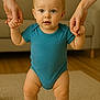 adult_hands, baby, carpet, child, cute, expression, face, floor, foot, hands, indoor, infant, leg, living_room, onesie, person, skin, support, toddler, walking