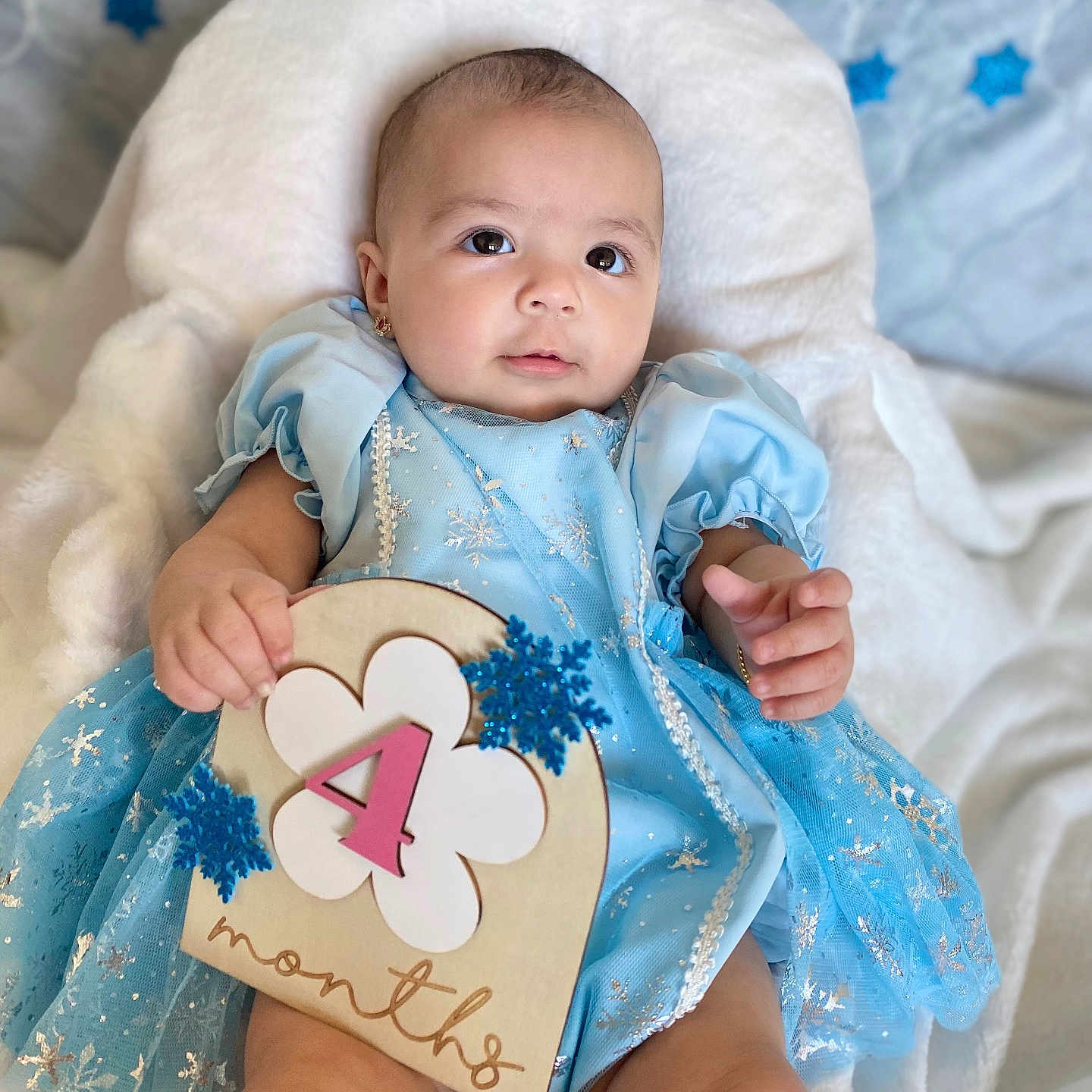 Samadhi is registered to the contest to win money with this photo: 4_months, baby, blanket, blue_dress, celebration, child, chubby, cute, earrings, foot, hand, head, indoor, infant, lying_down, portrait, sign, smiling, snowflake, soft_texture