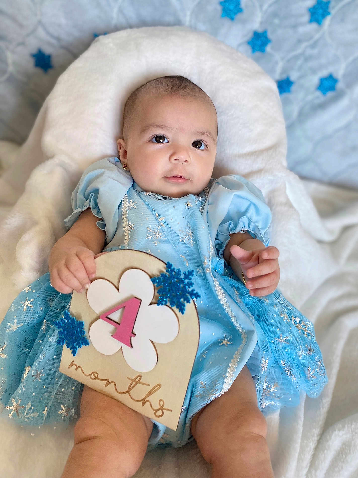 Samadhi is registered to the contest to win money with this photo: baby, infant, blue_dress, snowflake, sign, 4_months, blanket, cute, portrait, child, smiling, soft_texture, lying_down, earrings, chubby, celebration, indoor, head, hand, foot