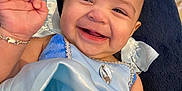 Samadhi is registered to the contest to win money with this photo: baby, child, smiling, blue_dress, bracelet, stuffed_animal, blanket, happy, portrait, person, infant, cute, fabric, toy, hand, face, indoor, closeup, joyful, accessory