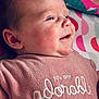 adorable, baby, child, close_up, clothing, cute, ear, face, happy, head, indoor, infant, patterned_background, person, pink_sweater, portrait, skin, smiling, text_on_clothing, young