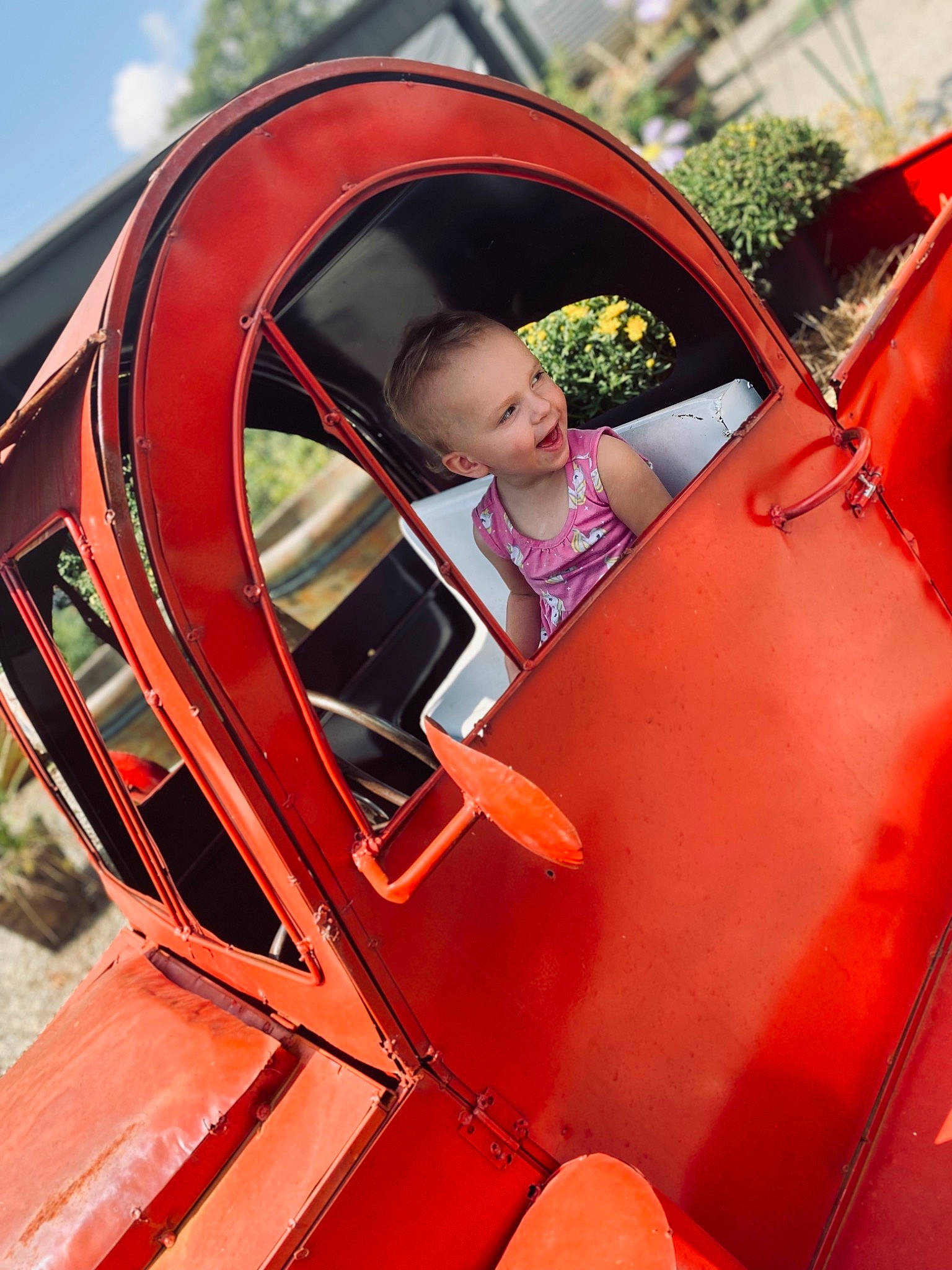 Adeline is registered to the contest to win money with this photo: automotive_design, automotive_exterior, automotive_lighting, automotive_wheel_system, bumper, car, fender, hood, jacket, magenta, motor_vehicle, orange, person, plant, rim, tire, toddler, vehicle, vehicle_door, wheel