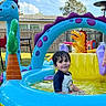backyard, blue, casual_clothing, child, dinosaur, fence, fun, grass, green, inflatable_pool, outdoor, play, purple, smile, summer, sunny, toy, water, wet_hair, yellow