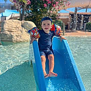 Ayann a rejoint le concours — aidez-le/la à gagner de superbes lots ! child, boy, water_slide, pool, floaties, blue_slide, water, summer, sunny, cap, swimwear, splash, outdoor, play, happy, nature, greenery, flowers, daylight, recreation