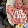 Evie is registered to the contest to win money with this photo: baby, sleeping, pink_sweatshirt, text_on_clothing, little_sister, colorful_pants, sun_print, animal_print, blanket, indoor, cozy, child, infant, resting, soft_fabric, cute, peaceful, person, clothing, casual